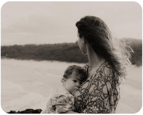 Mother and baby standing on beach looking out at ocean